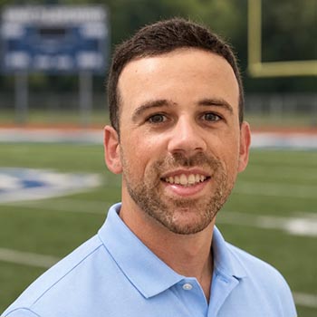 Portrait of a smiling man in a light blue polo on a football field
