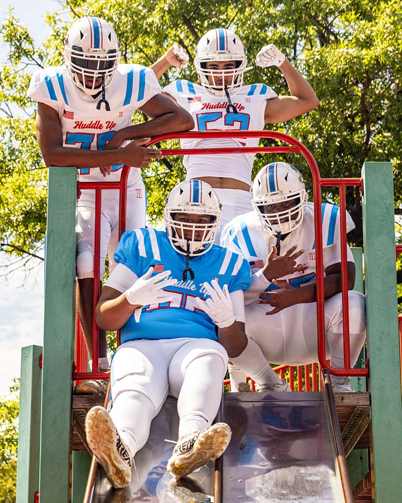 A youth football team posing on a playground slide with players in blue and white uniforms outdoors under trees